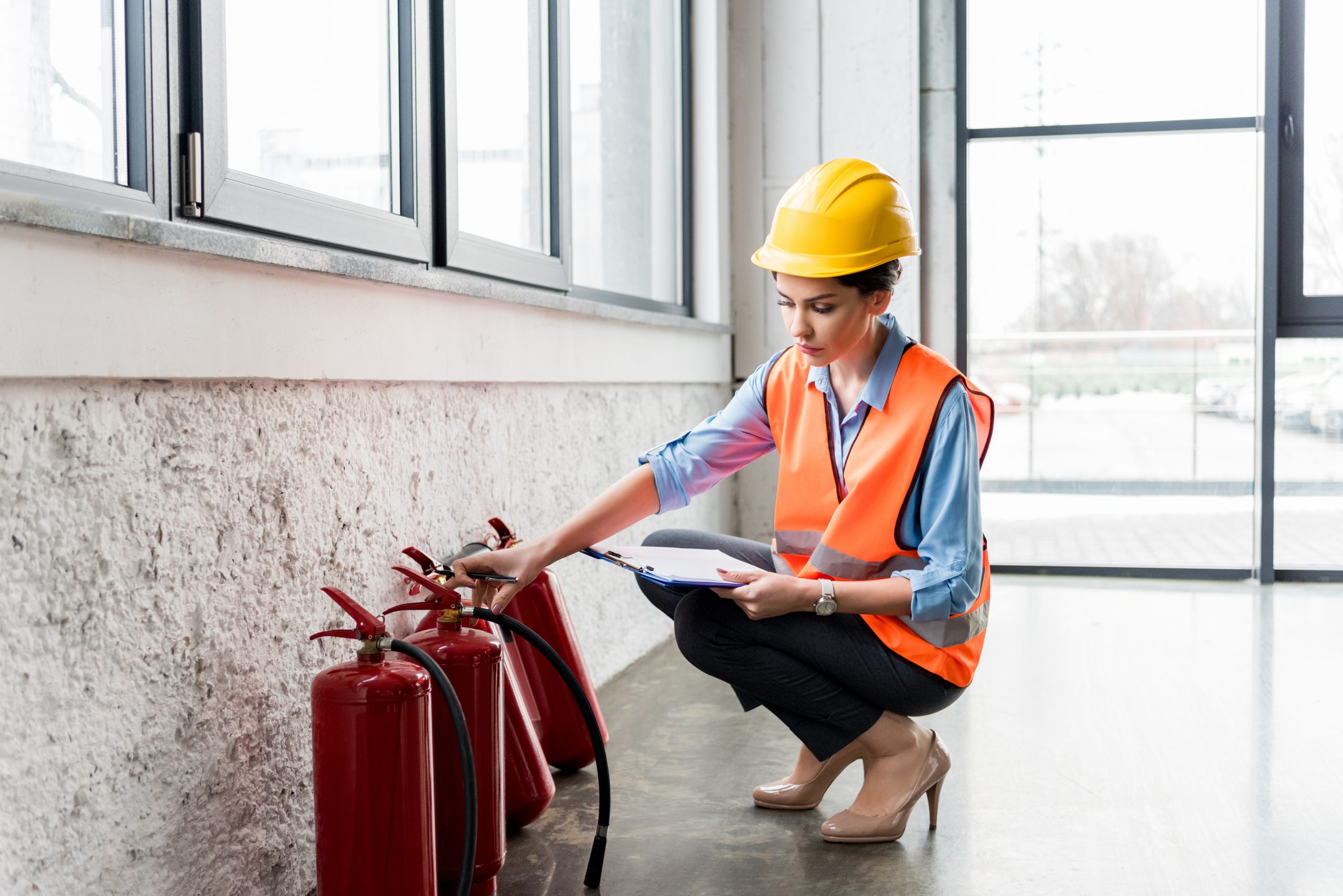 attractive firefighter in helmet holding clipboard and pen while checking extinguishers