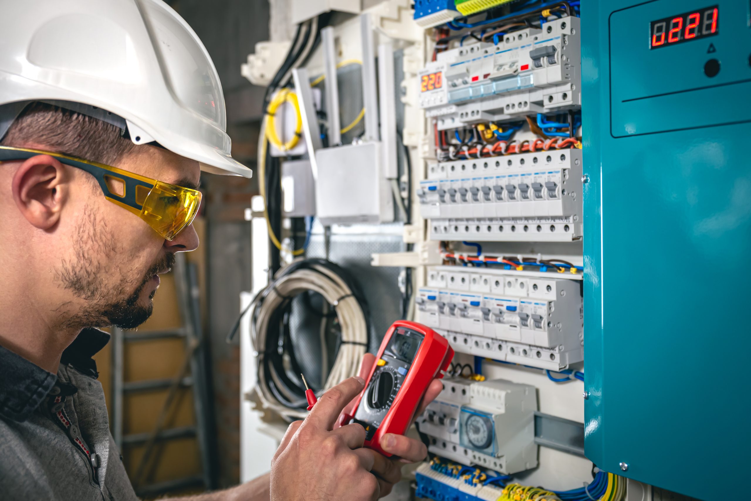 Man, an electrical technician working in a switchboard with fuses. Installation and connection of electrical equipment. Professional uses a tablet.